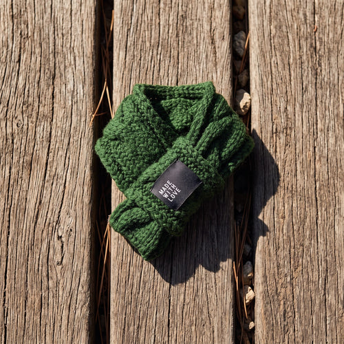 Close-up of thick cable-knit wool dog scarf styled on weathered oak surface, highlighting knit pattern and wool texture.