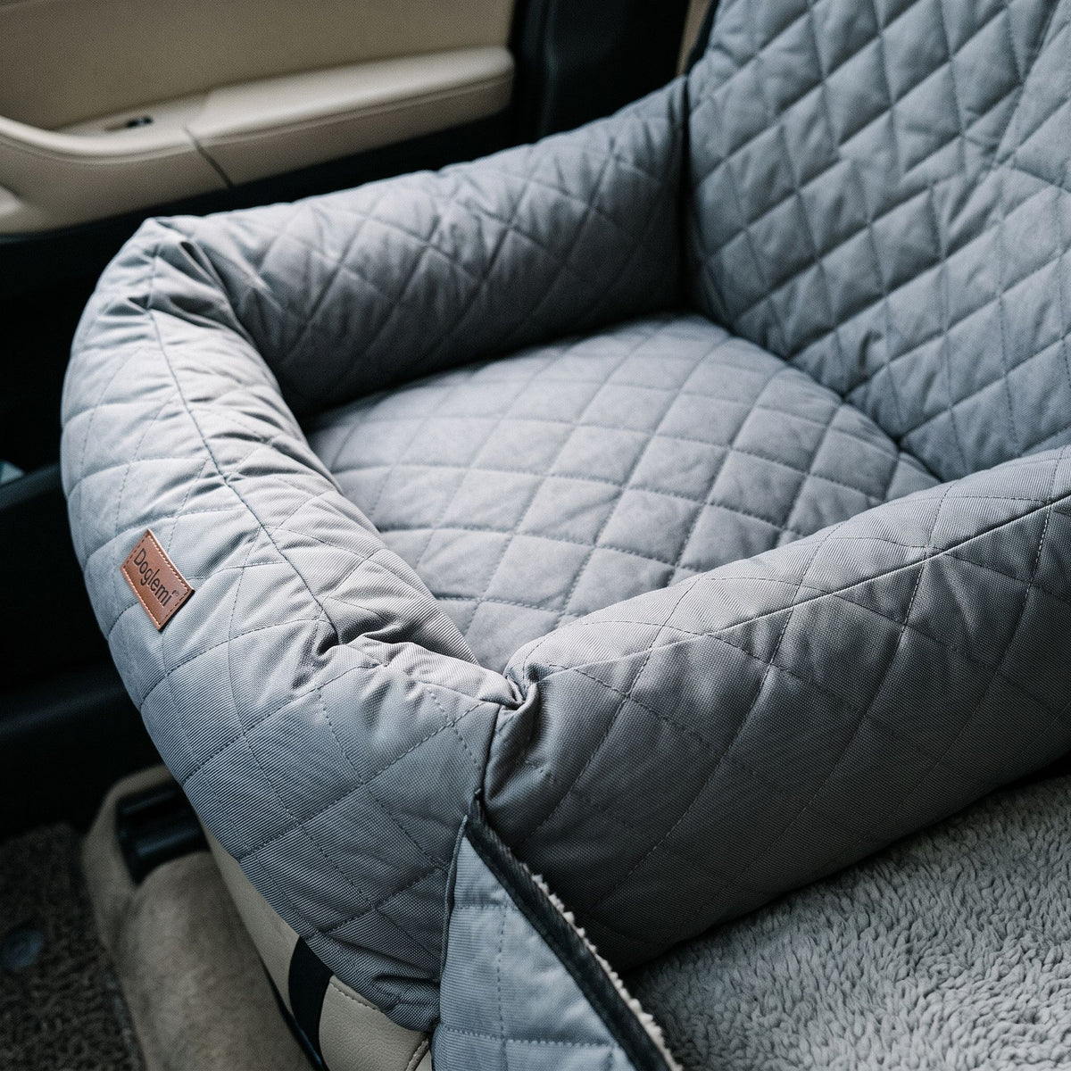 Close-up of quilted fabric and bolster of pet car bed showing stitching and texture under overhead car light.