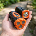 Macro shot of ultrasonic dog repeller with flashlight held outdoors, highlighting front speaker grille and flashlight in daylight.