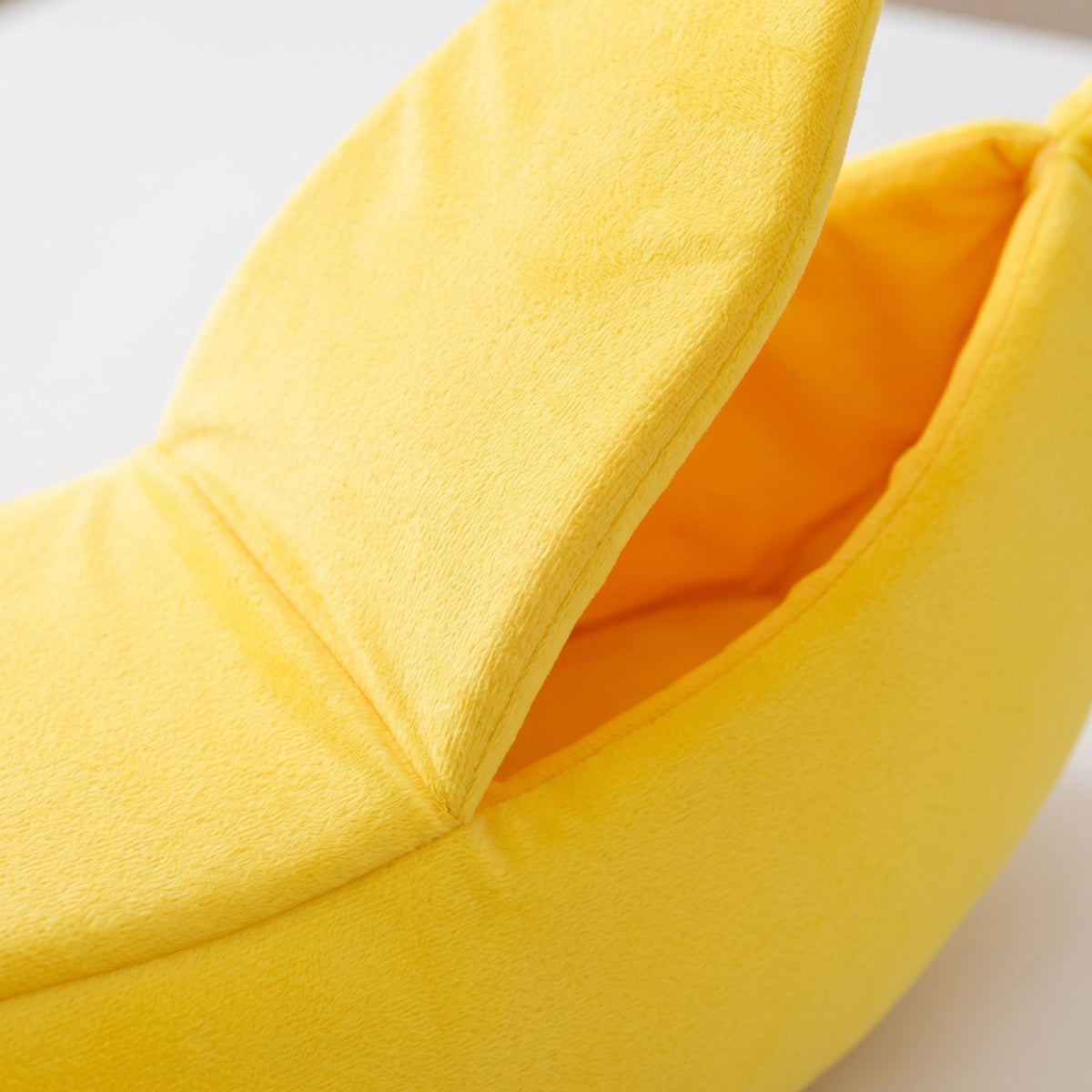 Detailed macro shot of the banana pet bed's peel-back flap showing velvet texture and stitching, white background.