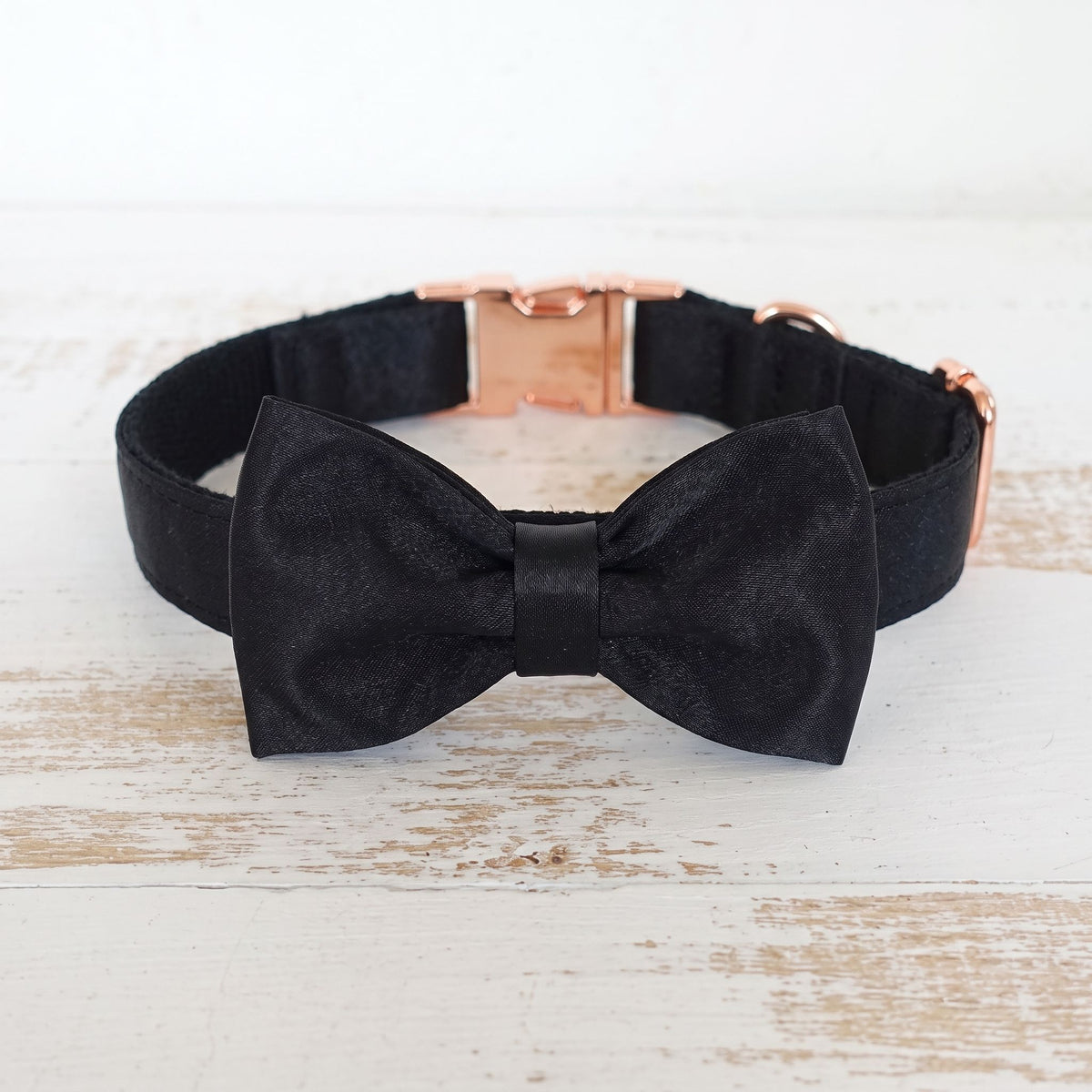 Dog collar with black bow tie and metal buckle on a light wooden surface, focused on the bow and hardware.