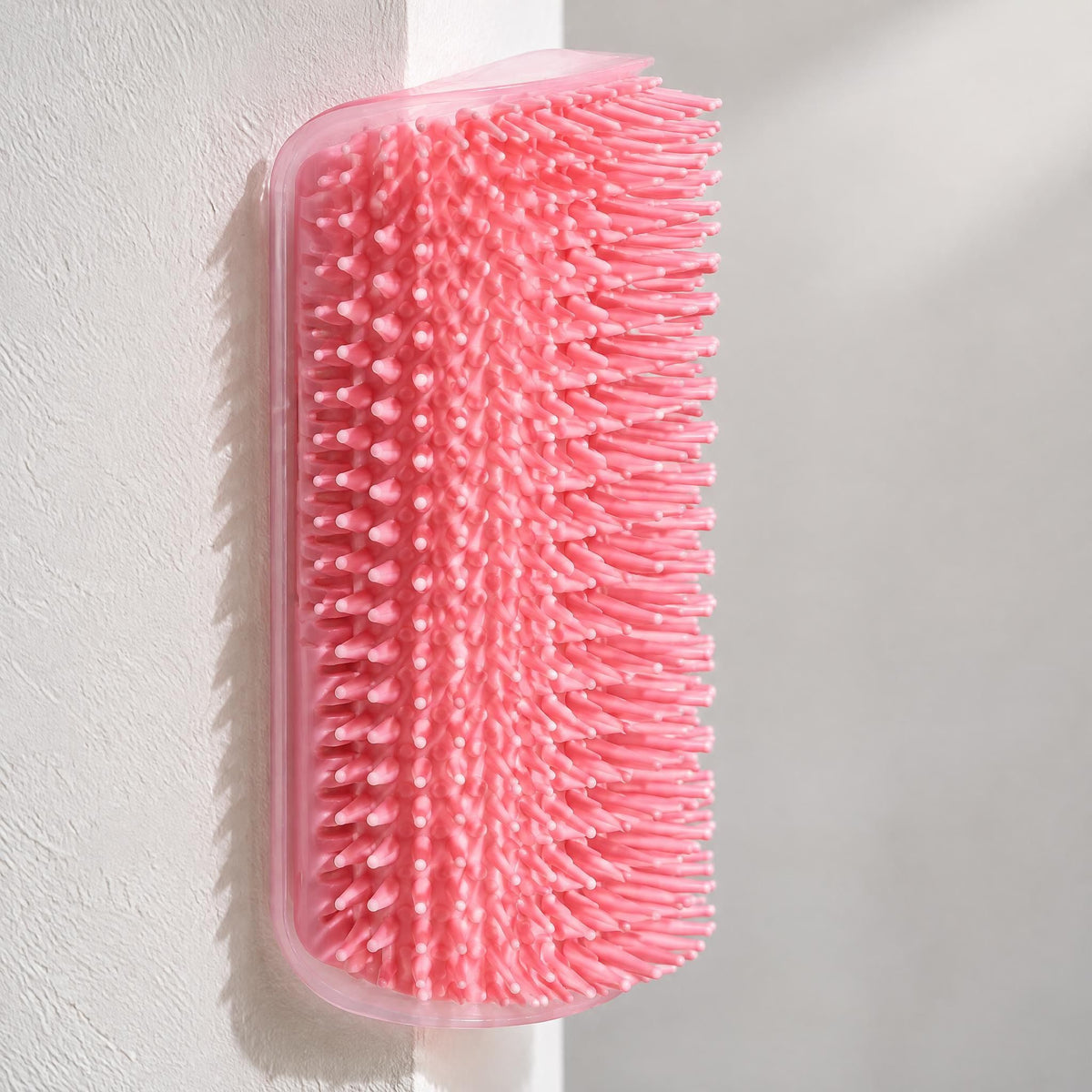 A pink silicone cat self-grooming brush mounted to a painted interior wall.