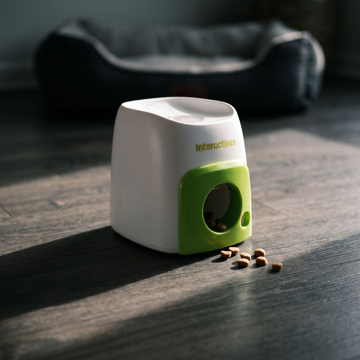 Interactive baseball treat dispenser on a dark wooden surface with a pet bed in the background.