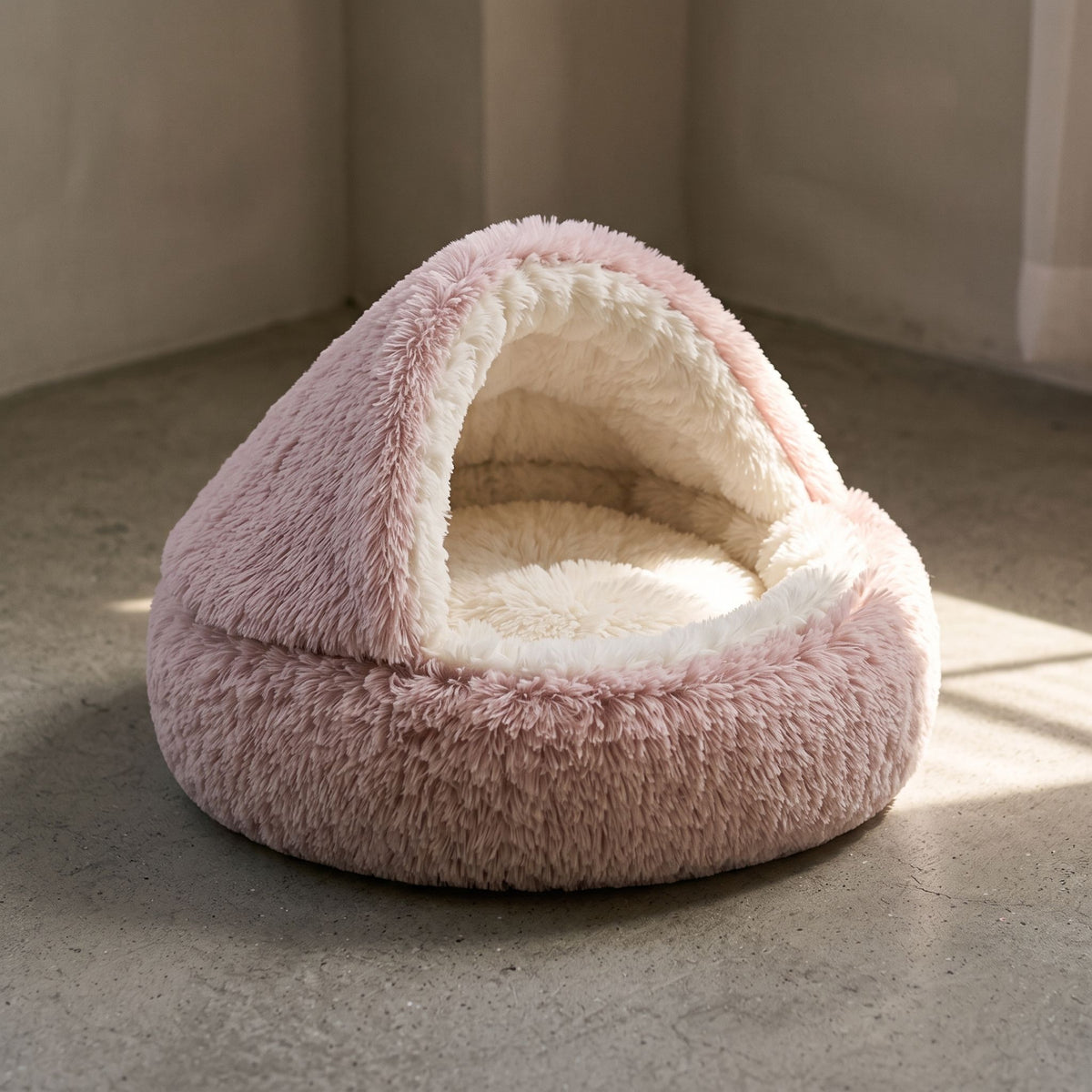 Semi-enclosed plush pet bed with a rounded form resting on a sunlit concrete floor.