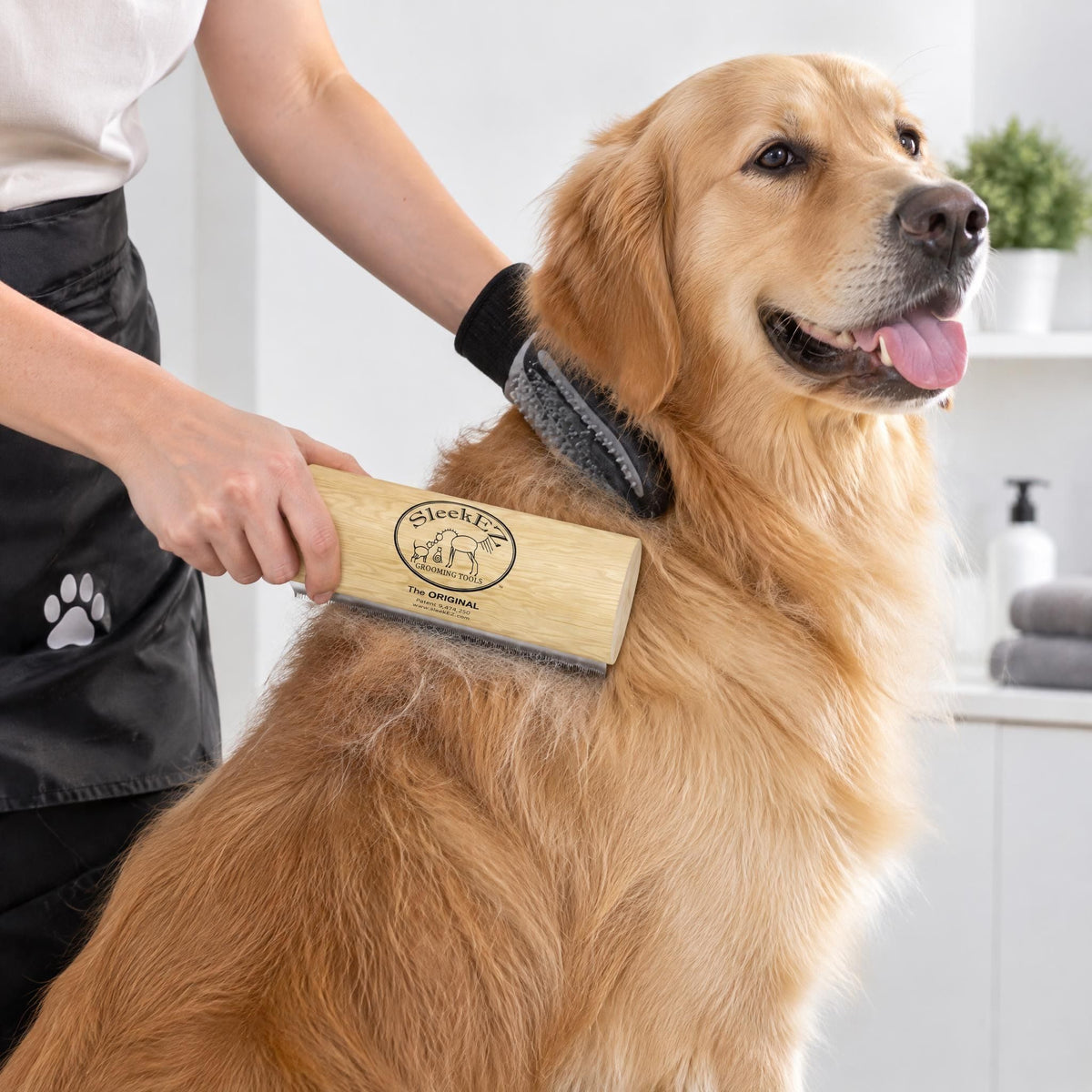 Person using a deshedding grooming brush on a pet to remove undercoat hair in a brightly lit room.