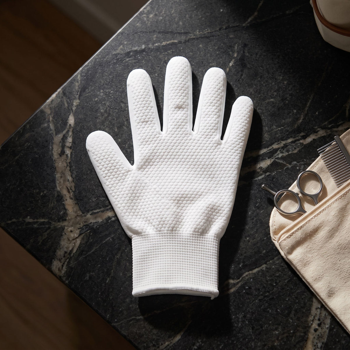 White disposable pet cleaning glove placed on a polished stone countertop next to a grooming kit.